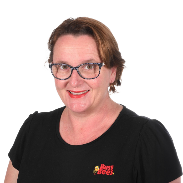 Tess Barry the Manager of Busy Bees Burpengary East, wearing glasses and a black shirt with a "Busy Bees" logo, smiling at the camera.